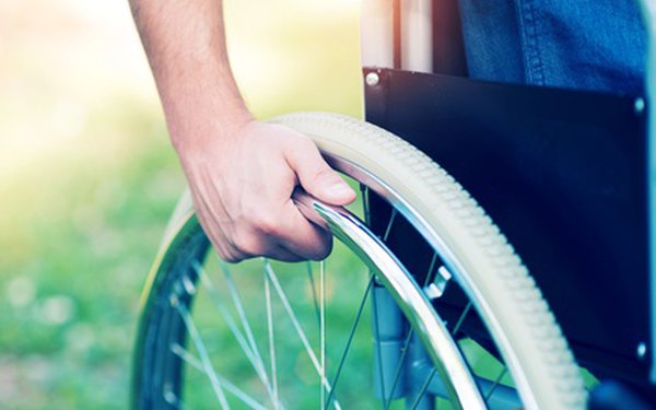 Eine Hand dreht das Rad eines Rollstuhls