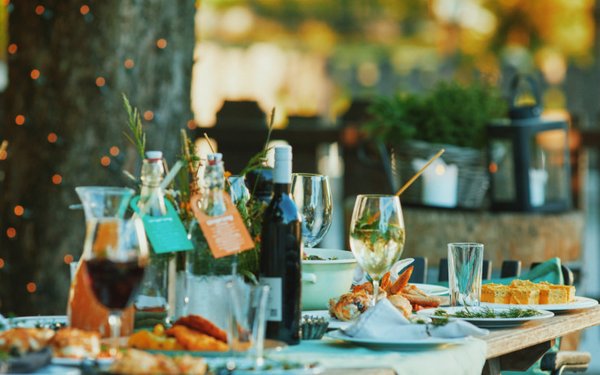 Ein reichlich gedeckter Tisch im Garten mit Wein, Aperitif und verschiedenen Speisen.