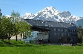 Das Gebäude des TBI-Grillhof von außen vor einer Bergkette, umgeben von Bäumen.