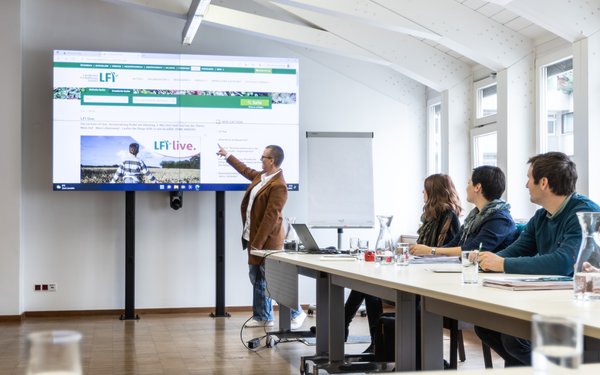 Heller Seminarraum mit Tischen, einer großen Leinwand und Flipchart.