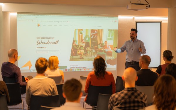 Vortrag im Souterain mit einer großen Leinwand und Reihenbestuhlung.