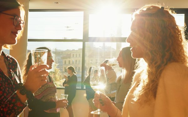 Frauen unterhalten sich, durch das Fenster der Stadtbibliothek strahlt die Sonne und erhellt die Weingläser.