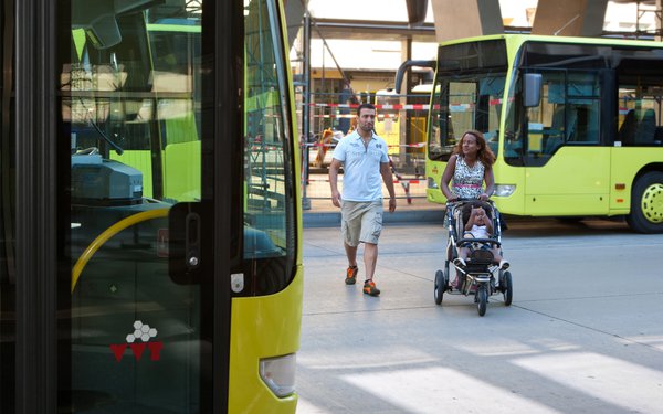 Frau mit Kinderwagen geht zu öffentlichem Bus