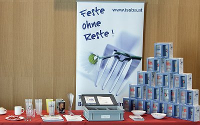 Ein Tisch mit issba-Mehrwegbechern. Dahinter hängt ein Banner mit dem Spruch "Feste ohne Reste!"